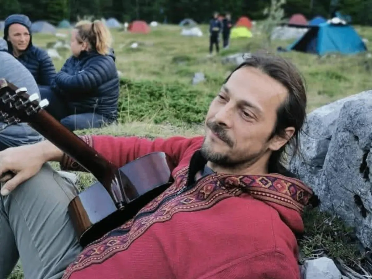Zoran Rončević, known as Ronac, reclining on grass with an acoustic guitar at an outdoor gathering.